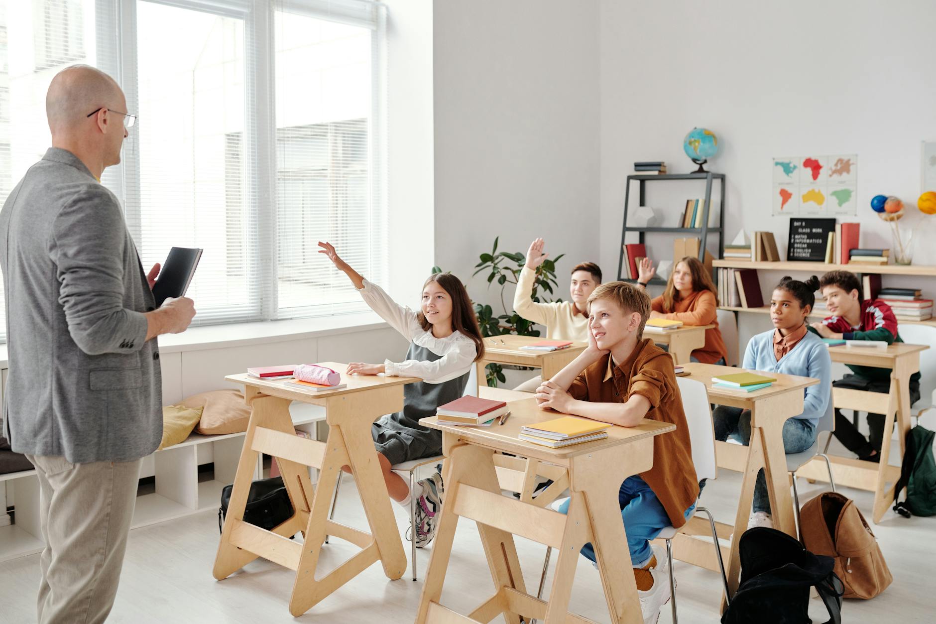 Young students sitting at desks in modern classroom with laptops and learning materials
