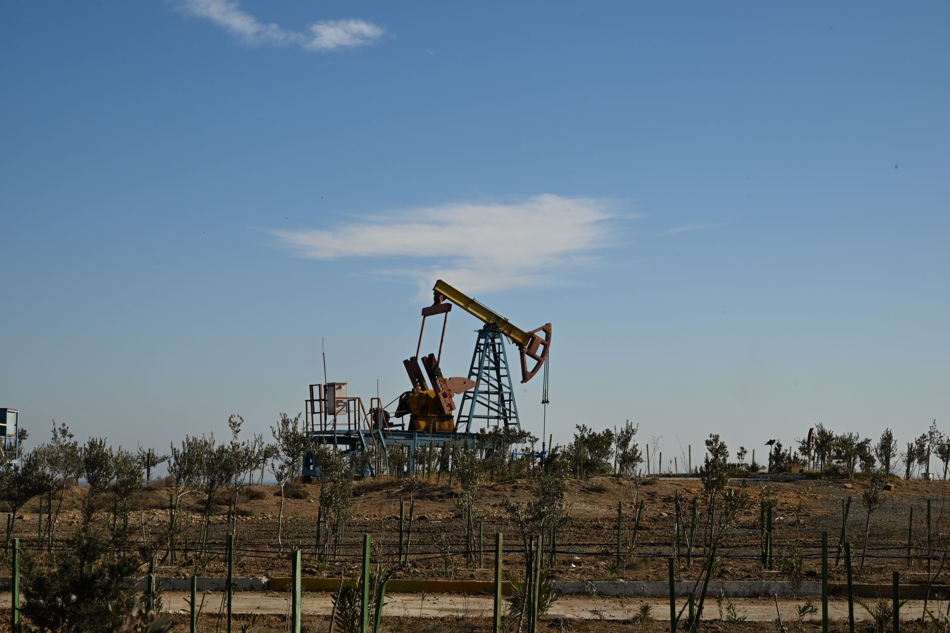 Industrial oil pump jack operating in an open field at sunset