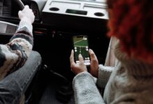 Person using a rideshare app on a smartphone while waiting on a city street