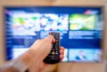 Person using a TV remote to browse a streaming service on a large screen