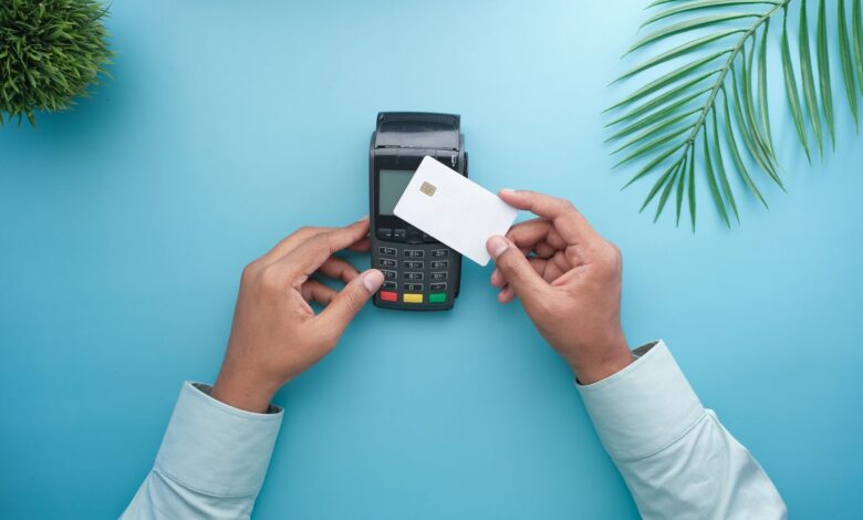 A customer tapping a credit card on a modern payment terminal at a small retail checkout counter
