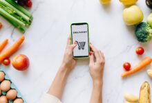 Person browsing a grocery delivery app on a smartphone while standing in a kitchen