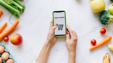 Person browsing a grocery delivery app on a smartphone while standing in a kitchen