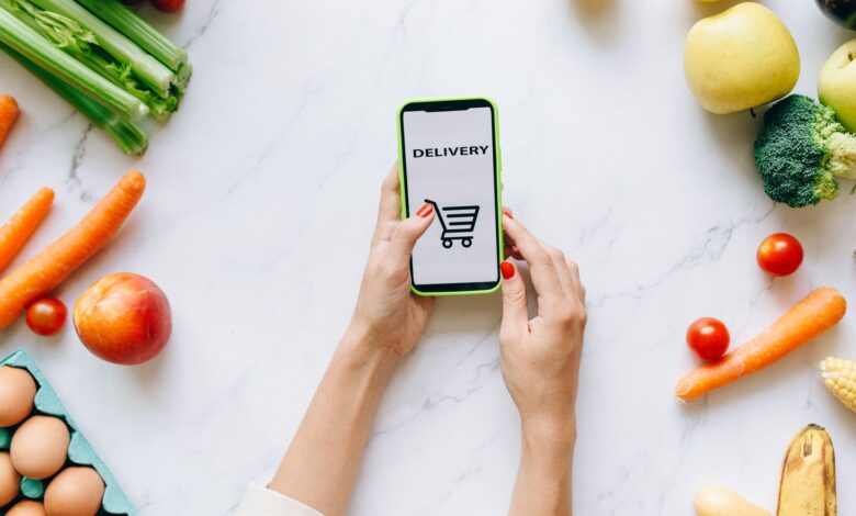 Person browsing a grocery delivery app on a smartphone while standing in a kitchen