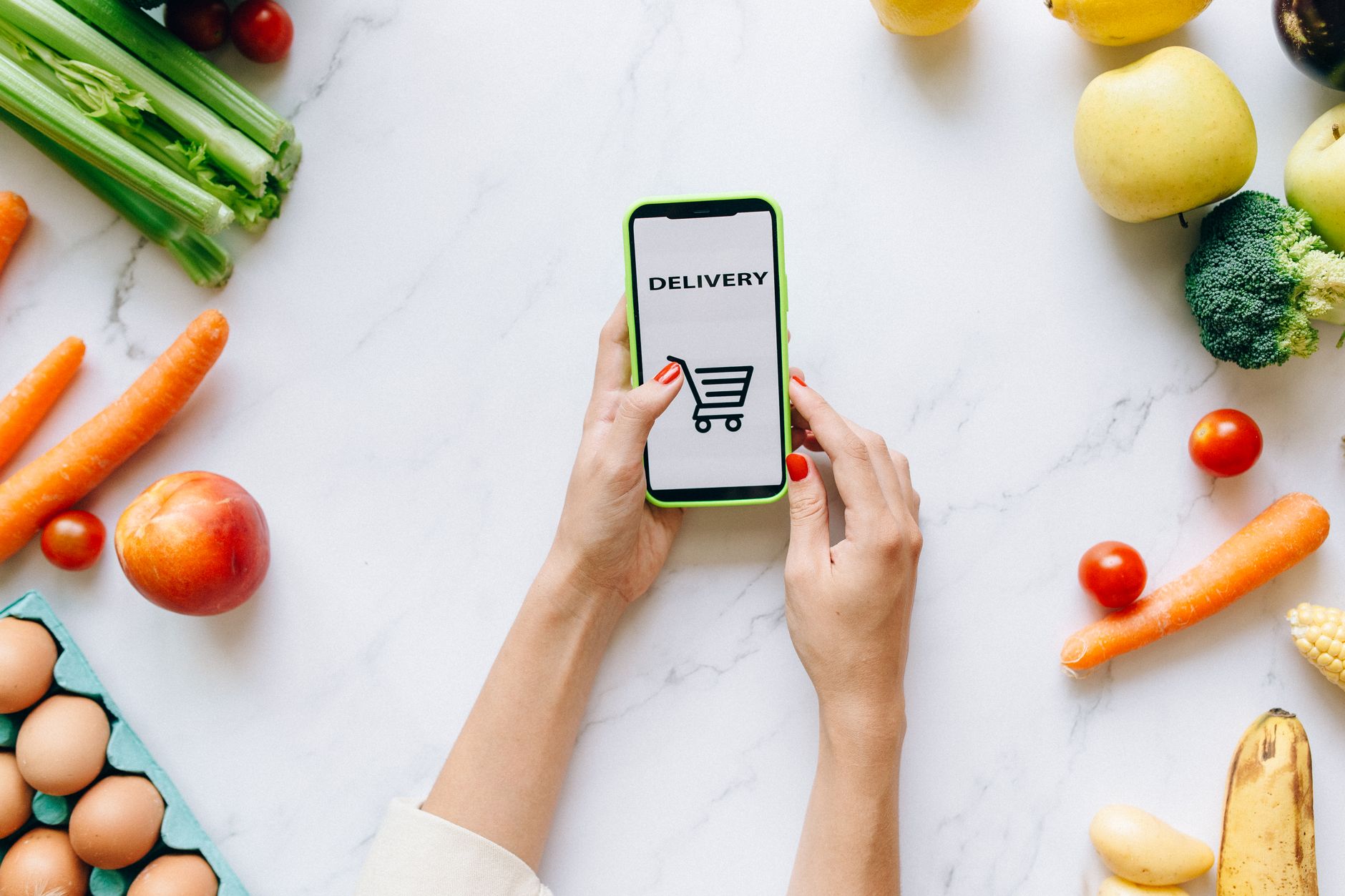 Person browsing a grocery delivery app on a smartphone while standing in a kitchen