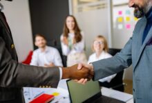 Two business professionals shaking hands over a signed contract representing a corporate operator deal