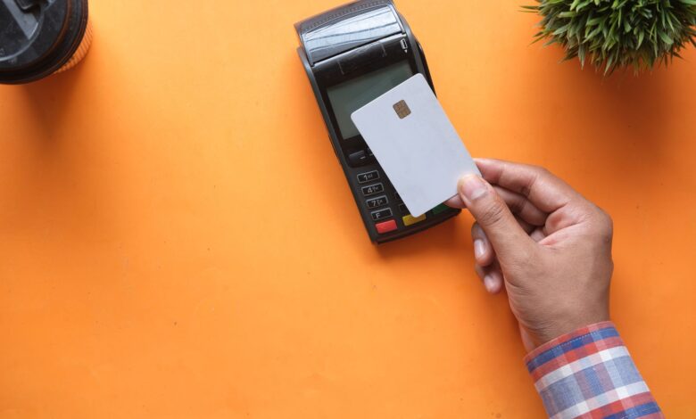 A shopper tapping a card on a contactless payment terminal at a retail checkout counter