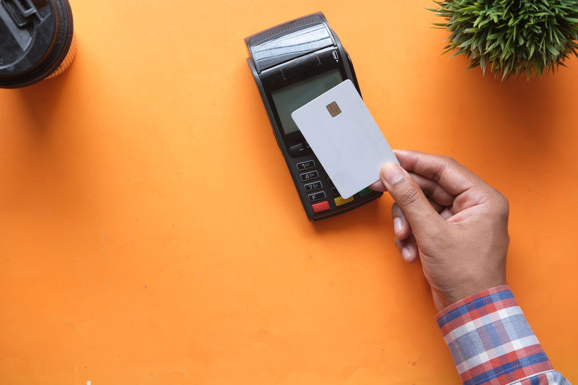 A shopper tapping a card on a contactless payment terminal at a retail checkout counter