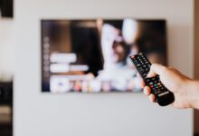 Person holding a television remote control while watching cable TV at home