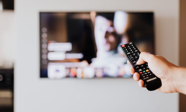 Person holding a television remote control while watching cable TV at home