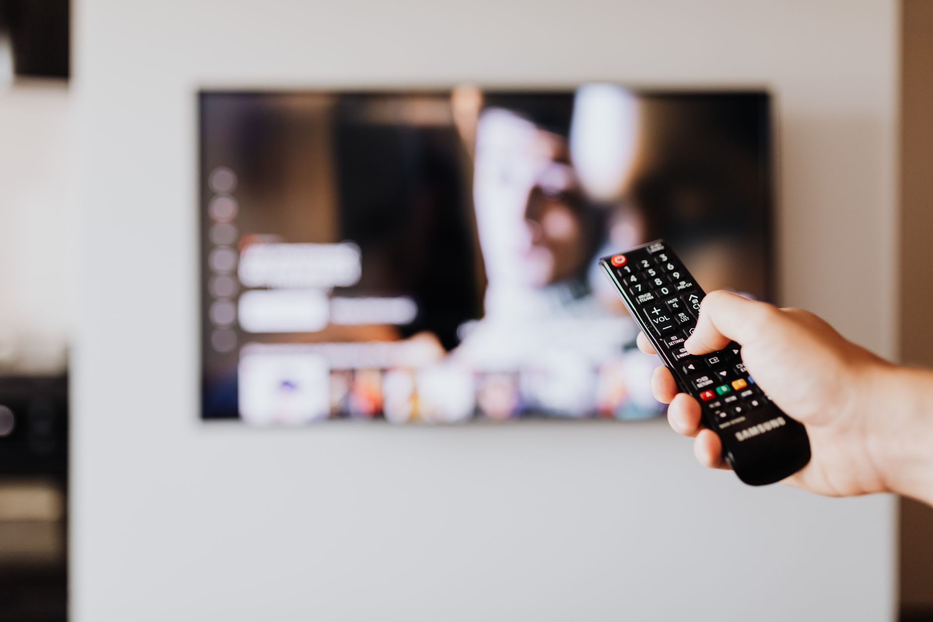 Person holding a television remote control while watching cable TV at home