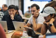 Software development team collaborating around a project management dashboard on a large monitor