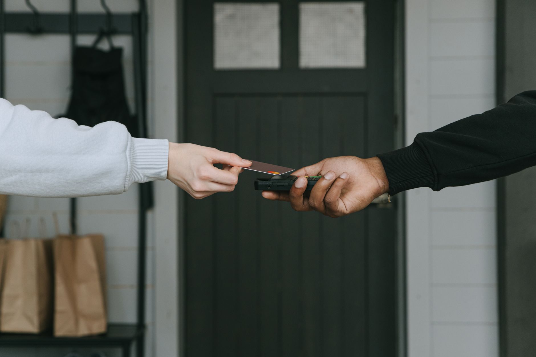 A hand holding a credit card near a modern point-of-sale payment reader